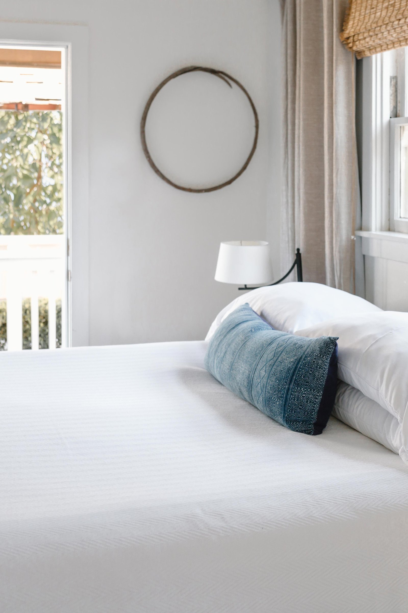 a room with white and blue bedding with an open door showing greenery and sunshine outside